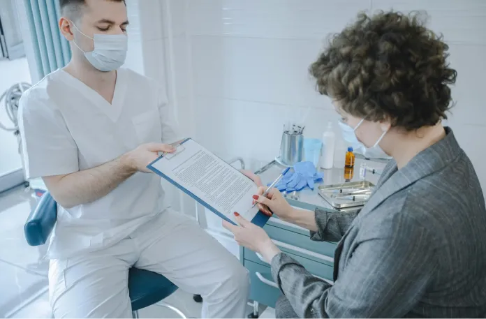 A man and woman converse over a document in a dental office, surrounded by dental equipment and a welcoming atmosphere.