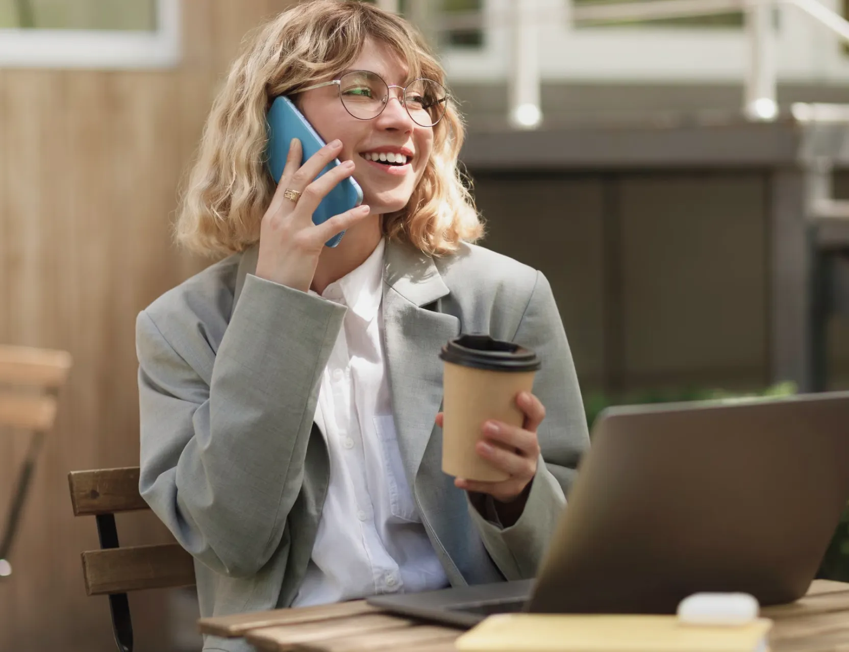 A professional woman in glasses and a suit, holding a coffee cup while engaged in a phone conversation.